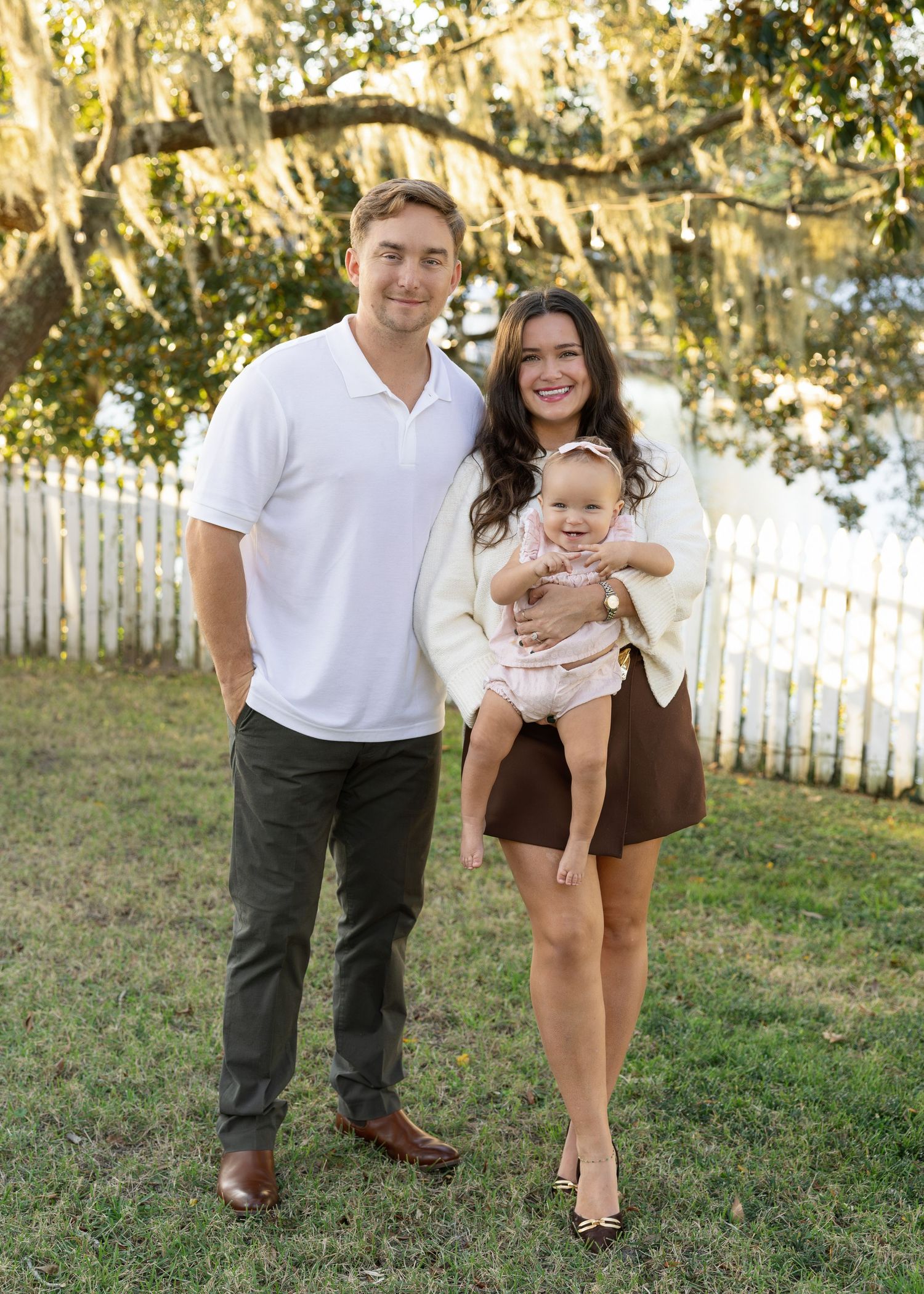 A couple playfully poses together in a series of candid shots on grass with a white picket fence in the background.