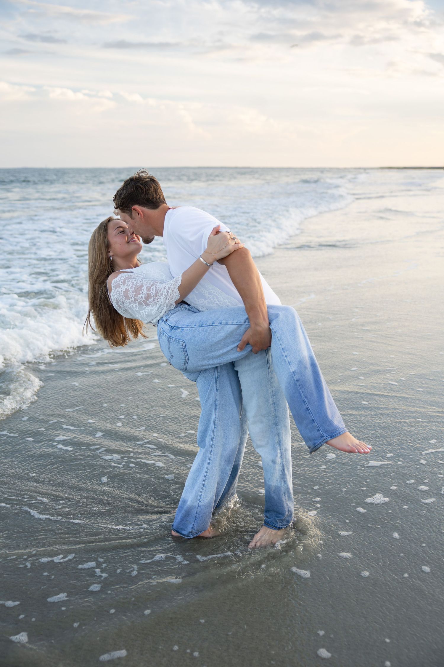 Romantic couple sharing a kiss on the beach at sunset, with ocean waves splashing around their feet.
