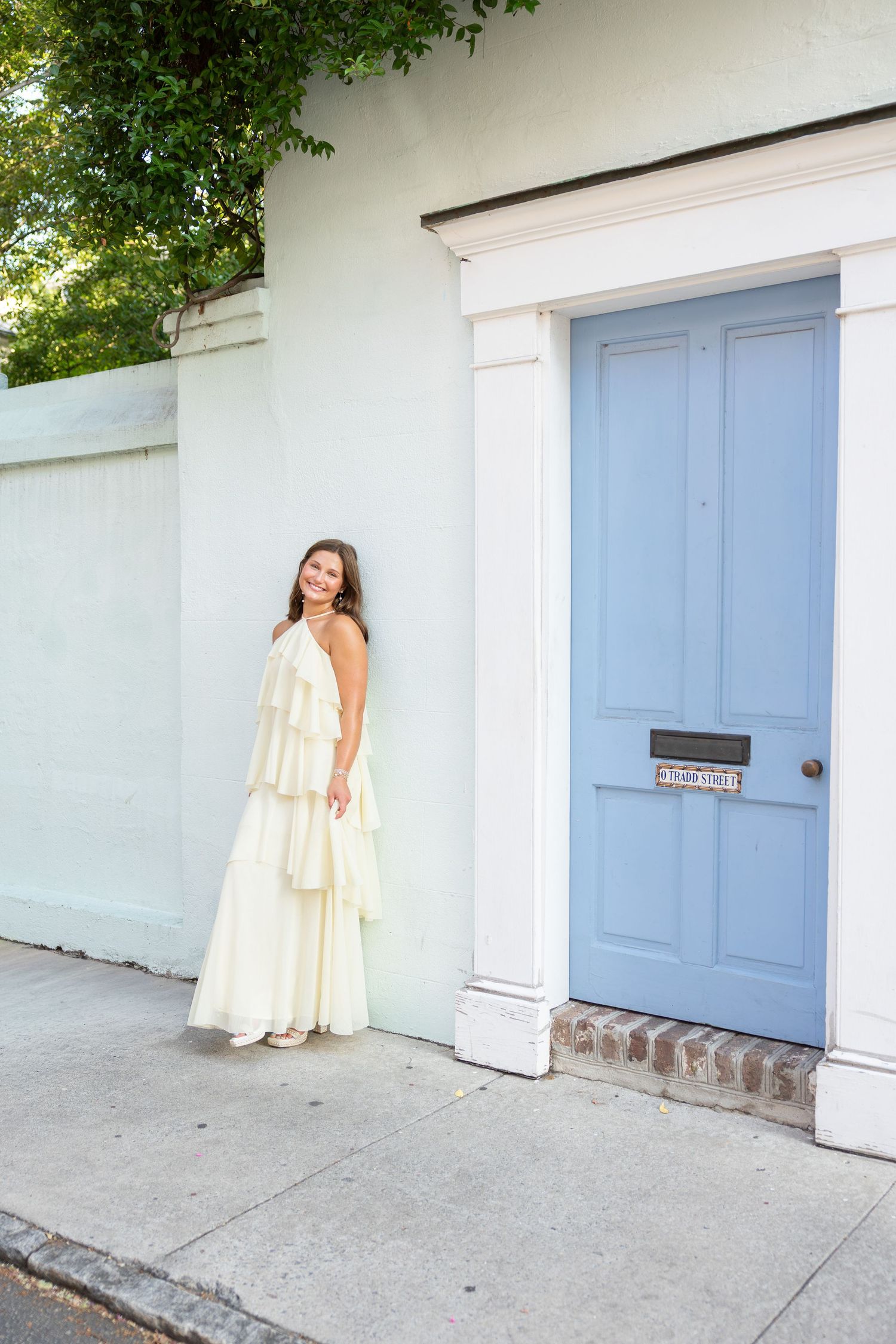 Woman in white tiered maxi dress posing beside a light blue door on a charming Charleston street.