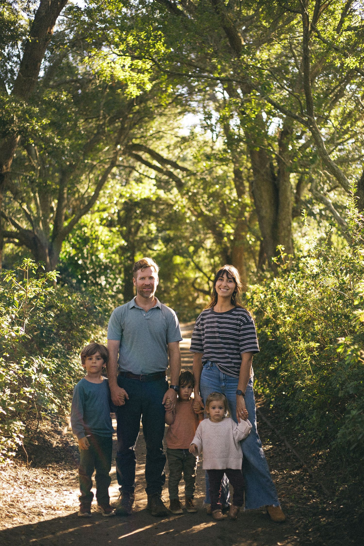 Owners of Charleston Outdoor Design stands together on a wooded path with sunlight filtering through autumn trees in the background.