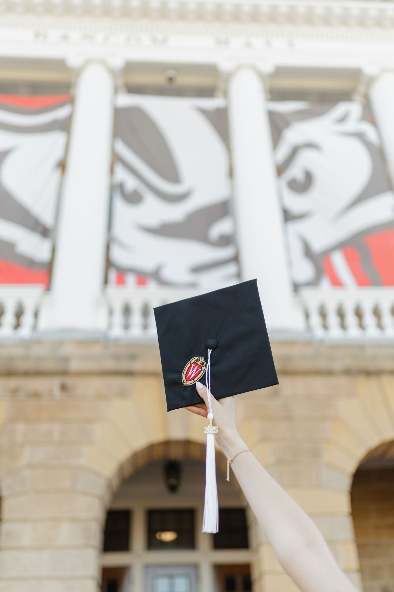 Black graduation cap thrown in the air against classical building columns and decorative wall art.