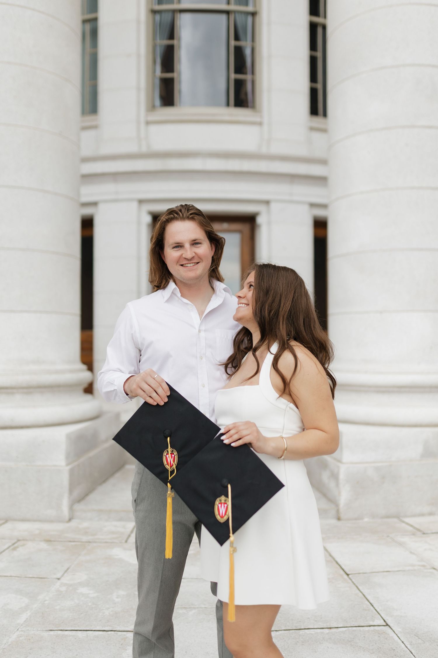 Graduate celebrates with cap and diploma in front of white columned building.