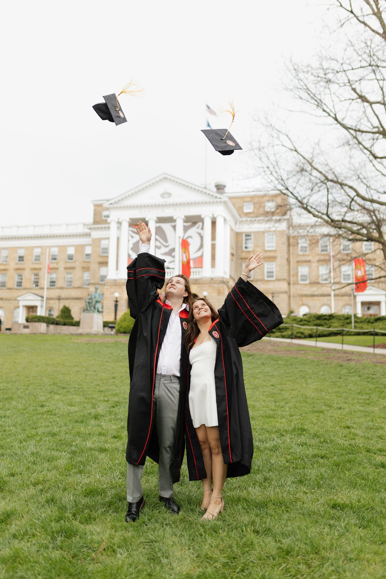 Graduates toss their caps in celebration on a grassy lawn in front of academic buildings.