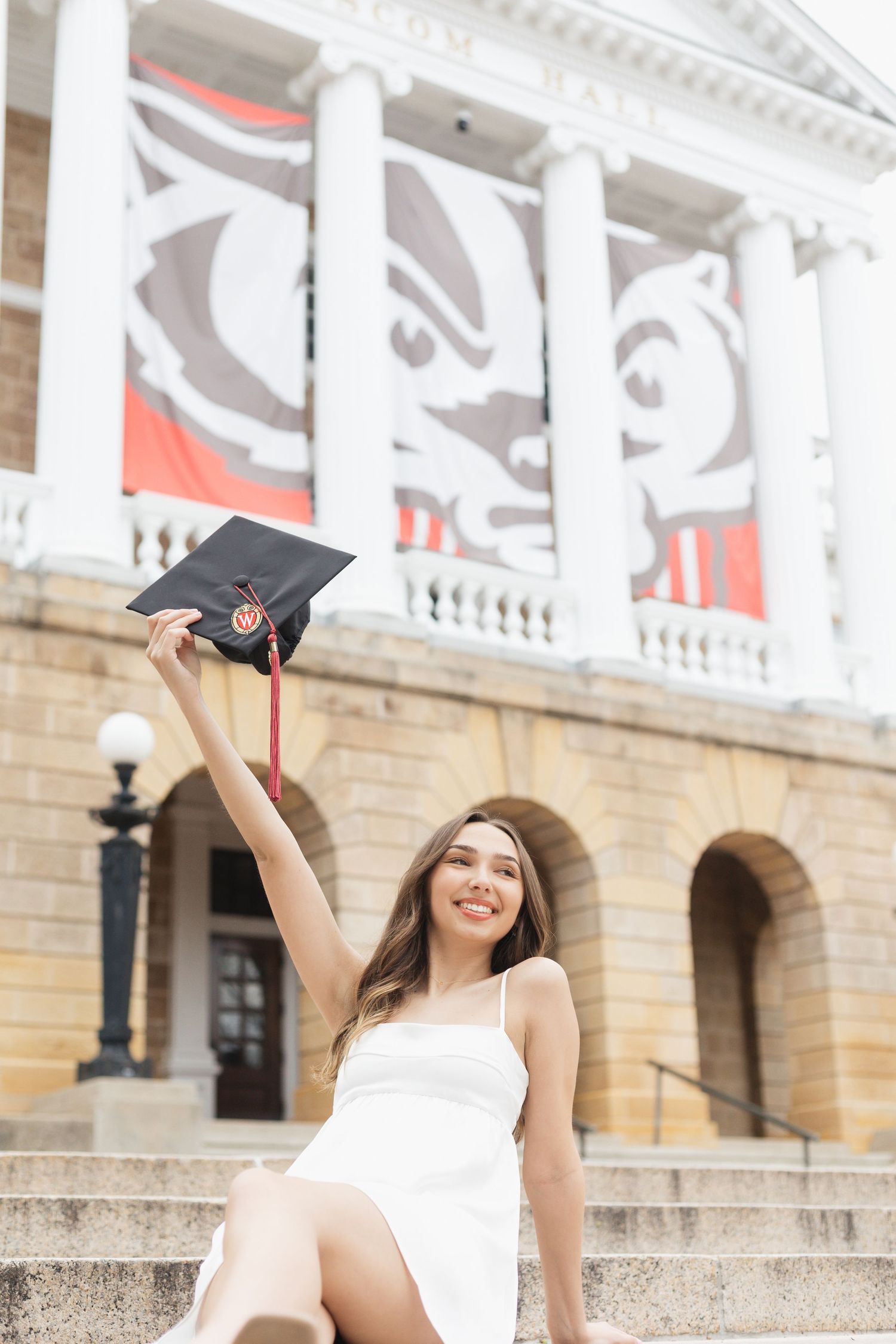 Graduate celebrates with cap toss on university steps with classical architecture.