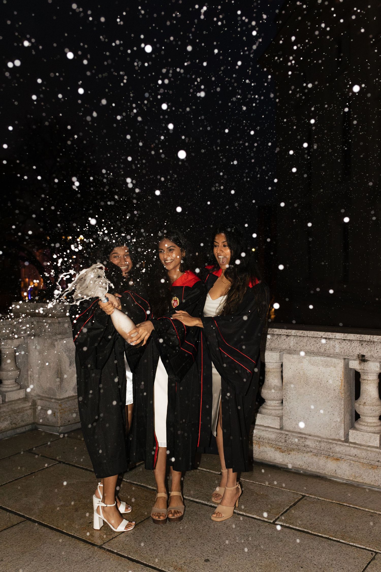 Group celebrating graduation at night with falling snow.