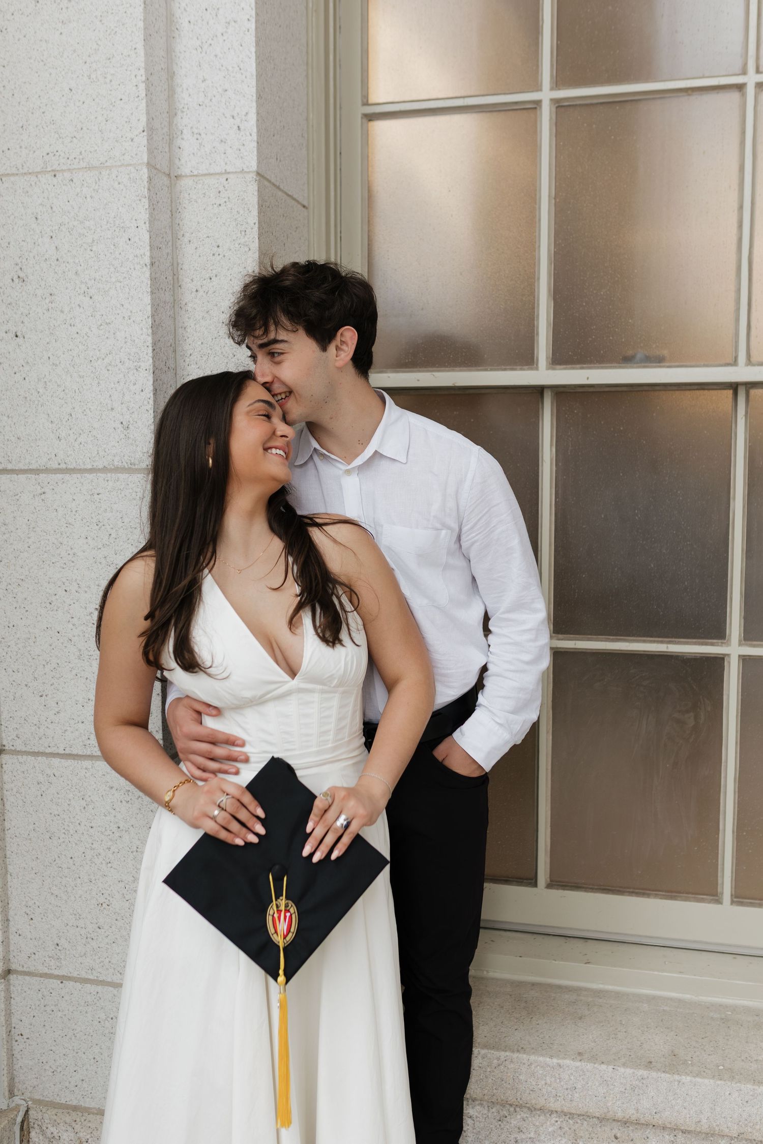 Graduates share intimate moment with decorated cap during graduation photoshoot.