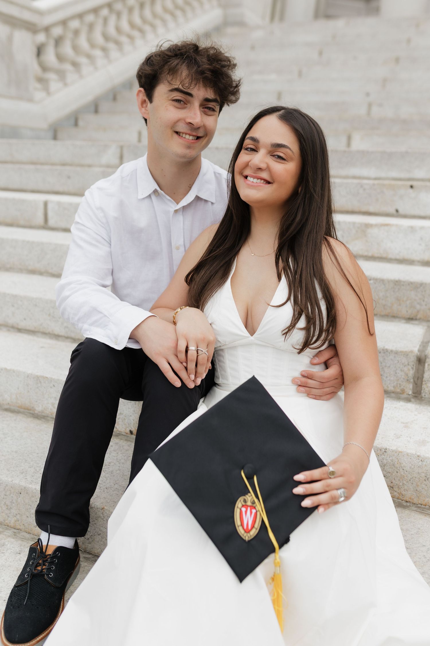 Graduates pose with decorated caps on white stone steps during graduation photoshoot.