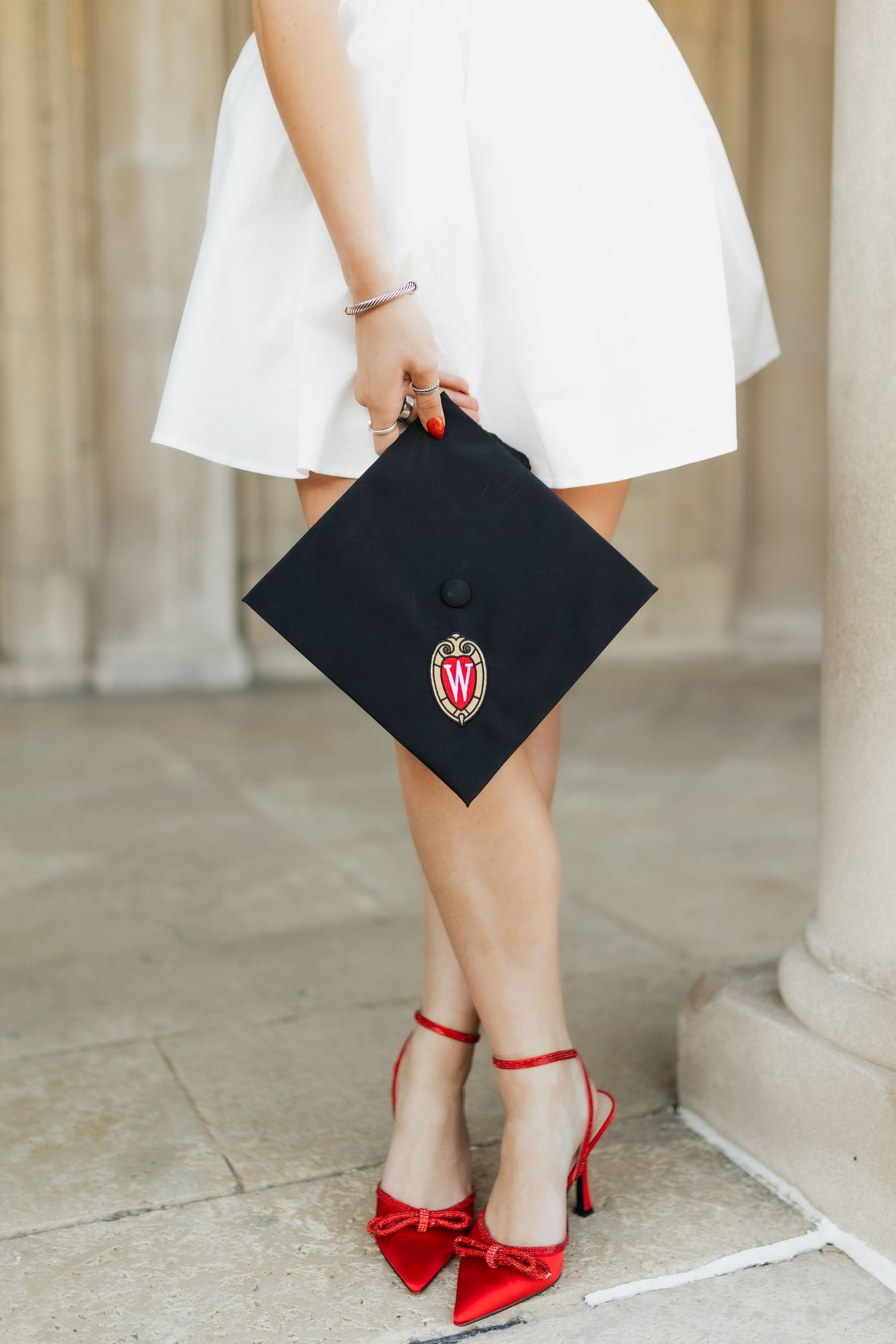 Close-up of graduate's red shoes and graduation cap with university logo.