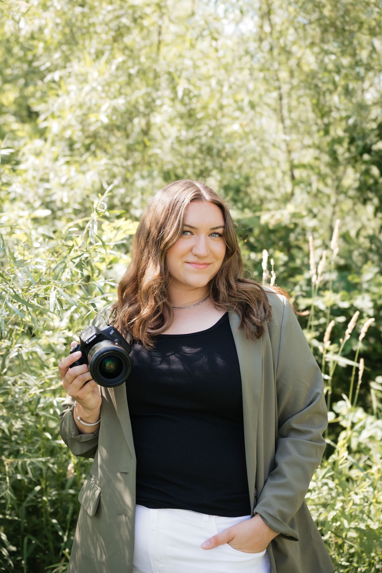 Casual outdoor portrait session in a green garden setting wearing a black top and olive jacket.