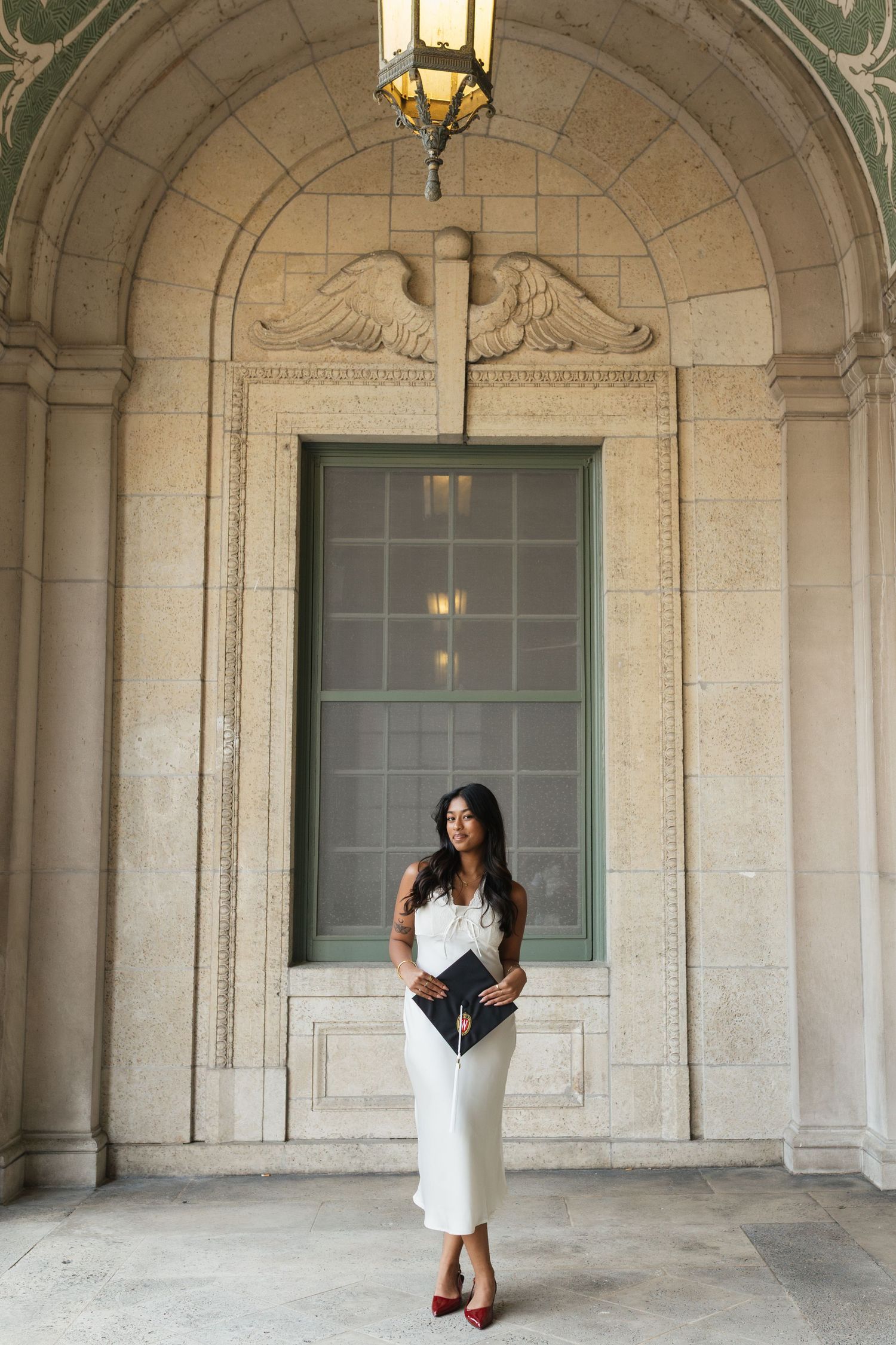 UW Madison graduate in white dress stands in Memorial Union archway,