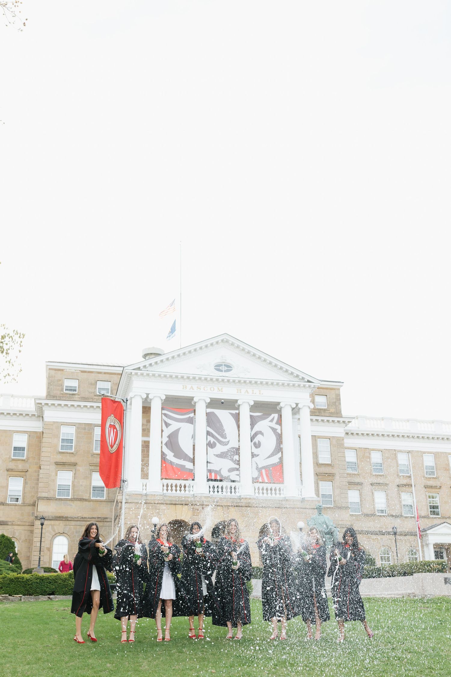 Graduates celebrate by throwing confetti in front of a grand university building.