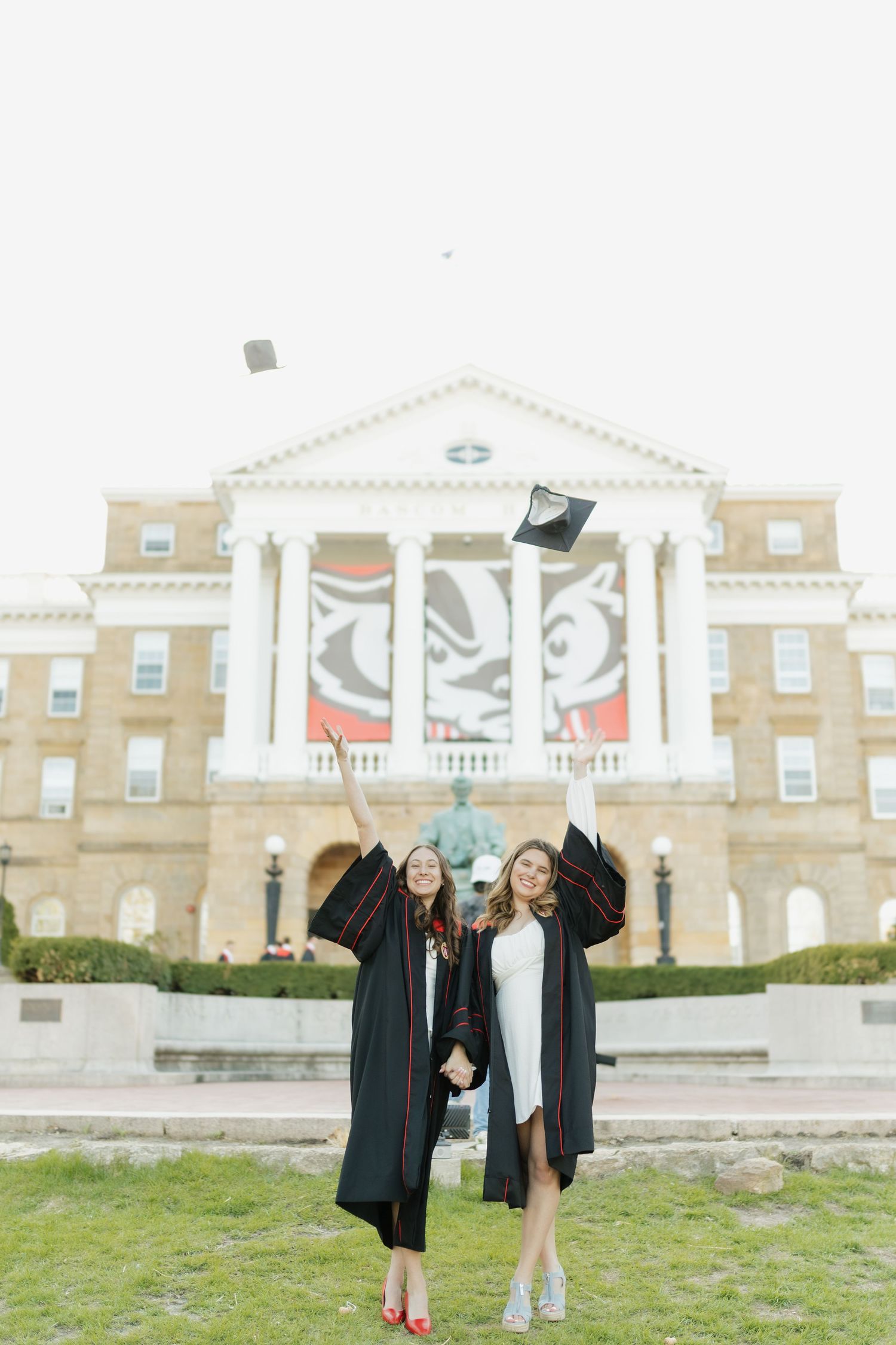 Graduates celebrate with caps in air in front of grand university building.