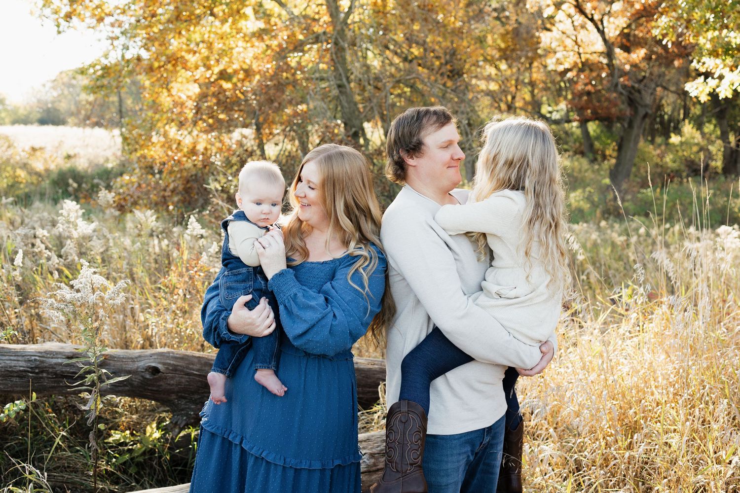 A family in coordinating navy and white outfits poses together in a golden autumn field during sunset.