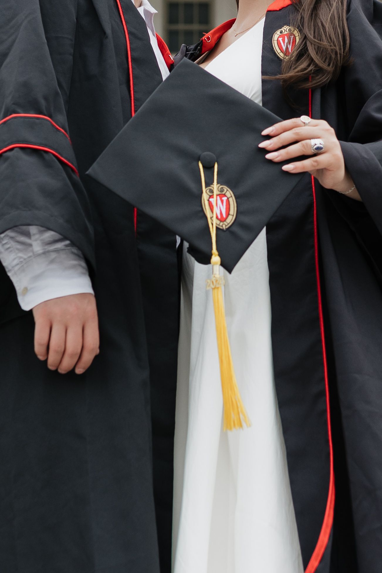 Close-up details of graduation gowns showing black fabric with red trim and gold tassels.