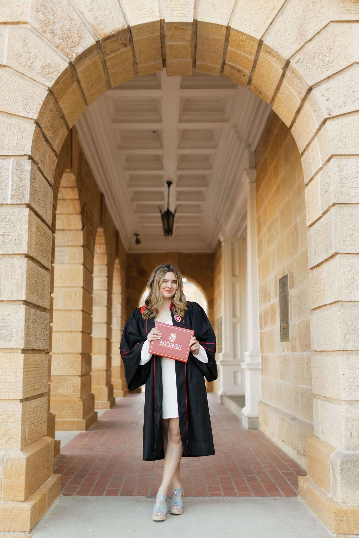 Graduates celebrate in black gowns under ornate stone arches of university building.