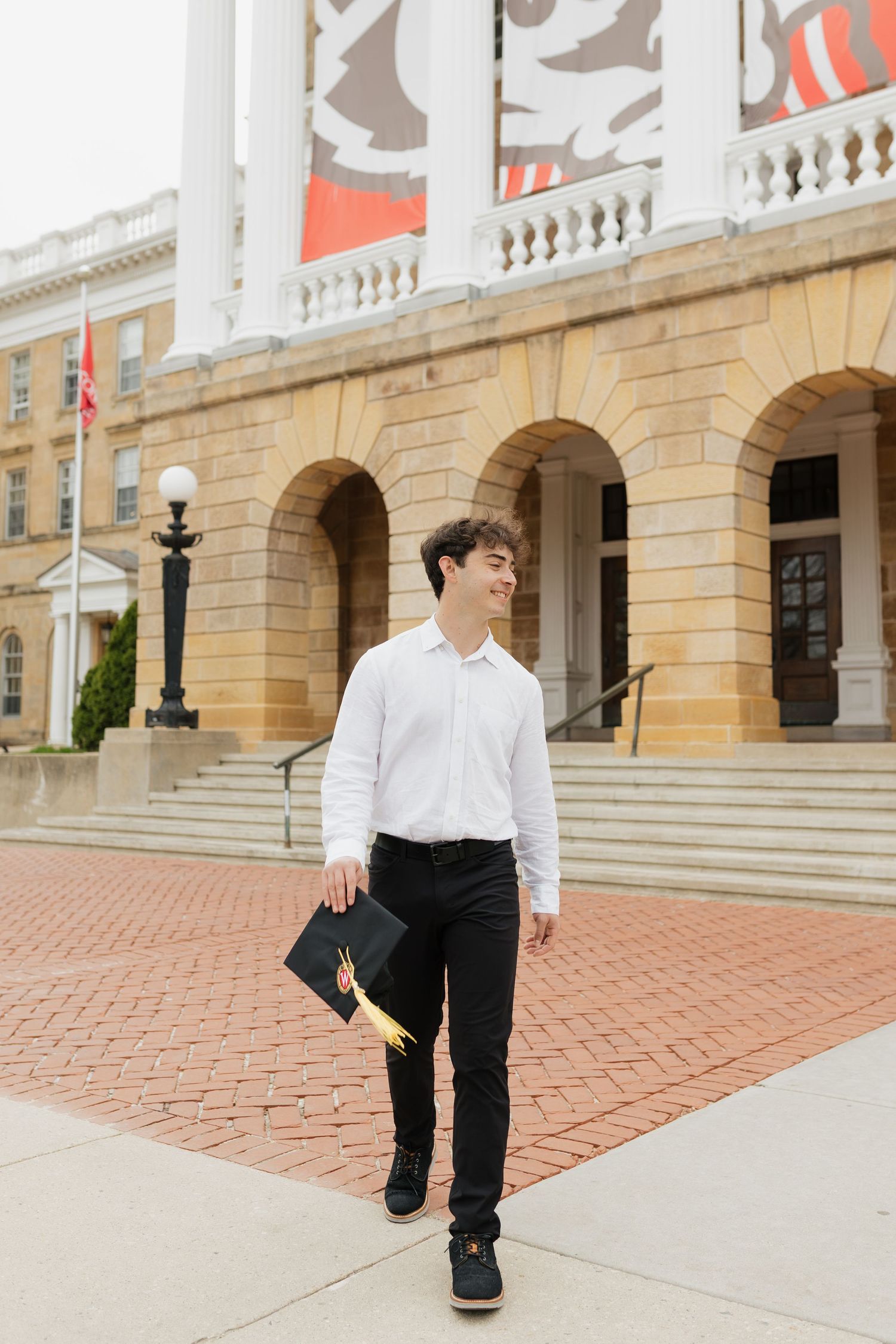 Playful graduation photo series on brick courtyard in front of classical building.