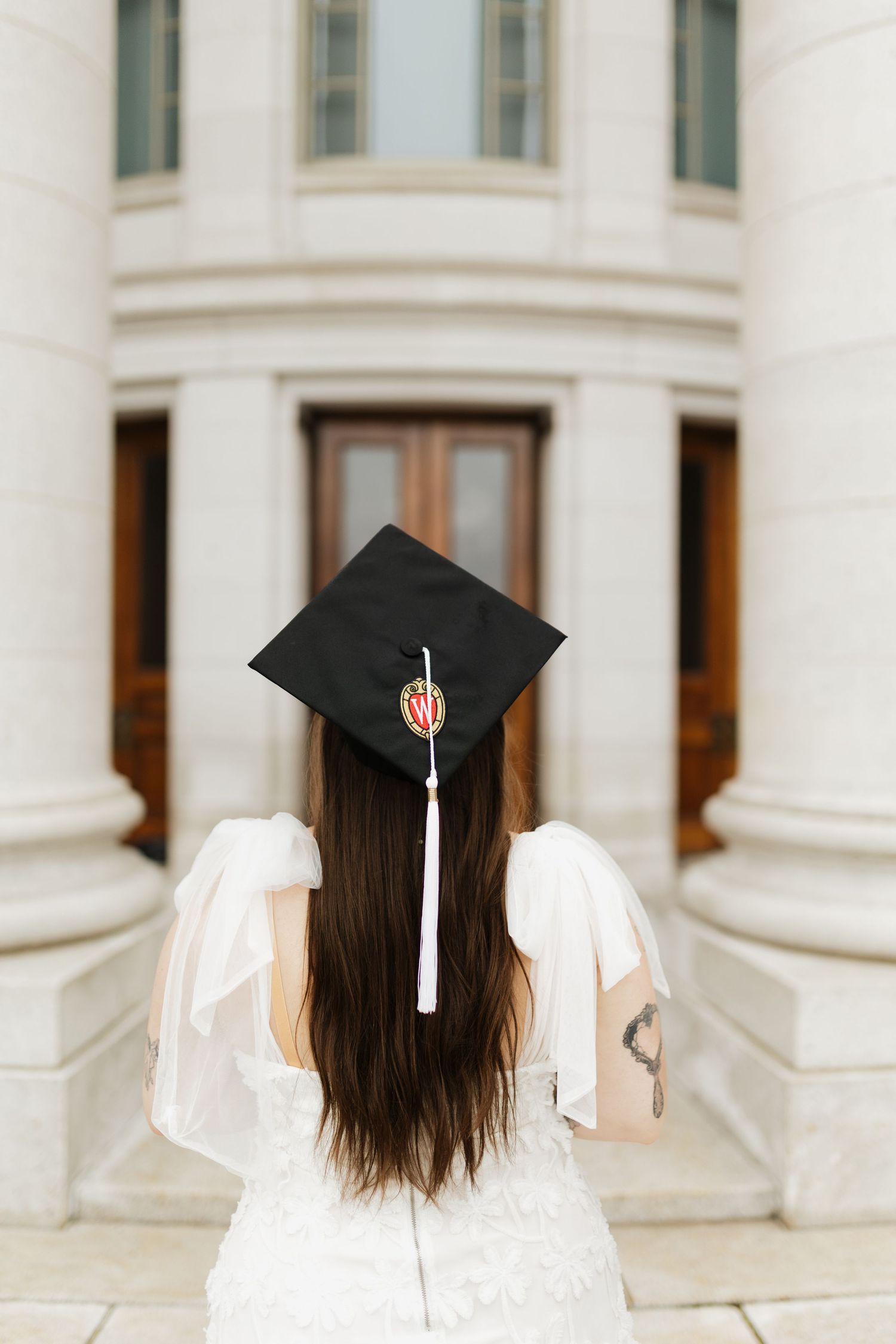 Back view of graduate wearing mortarboard against white columned building.