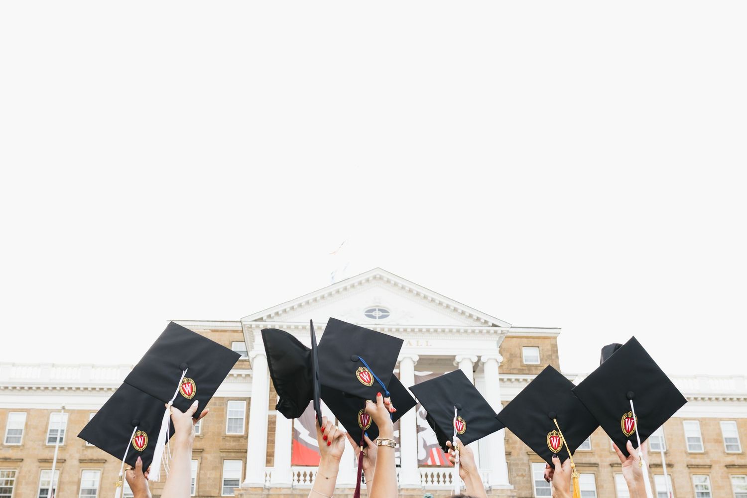 UW Madison graduation caps being thrown into the air against a building backdrop during a commencement ceremony celebration.