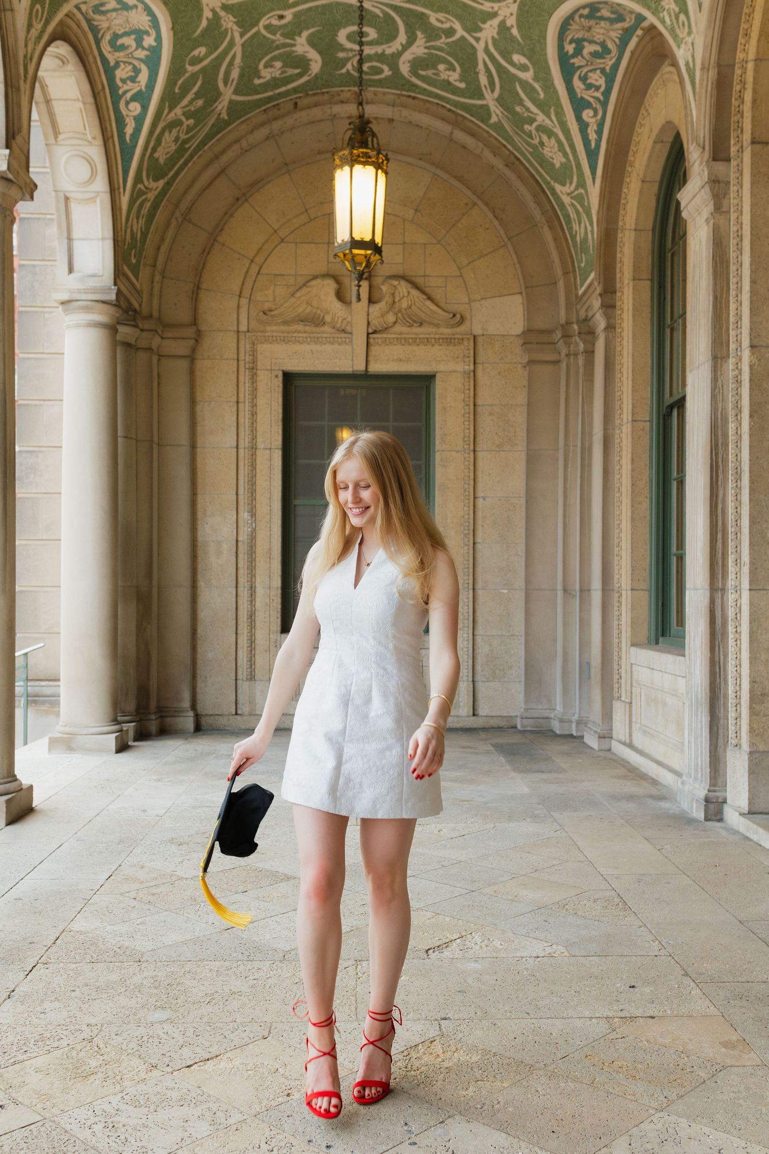 UW Madison graduate in a white dress and red sandals standing in Memorial Union Arches.