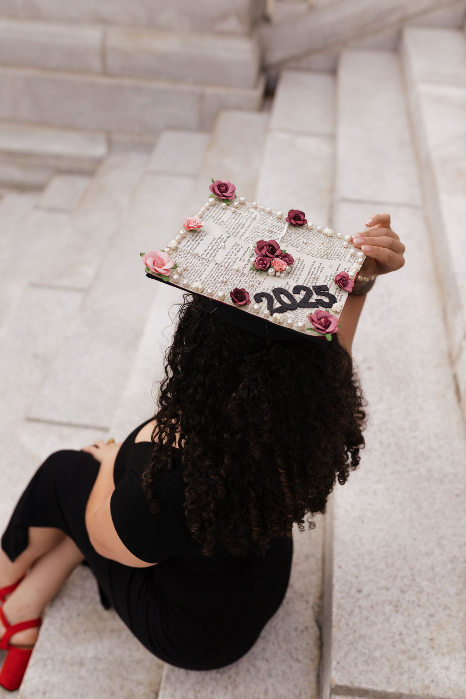 Graduate holding a decorated diploma cover while sitting on marble steps.