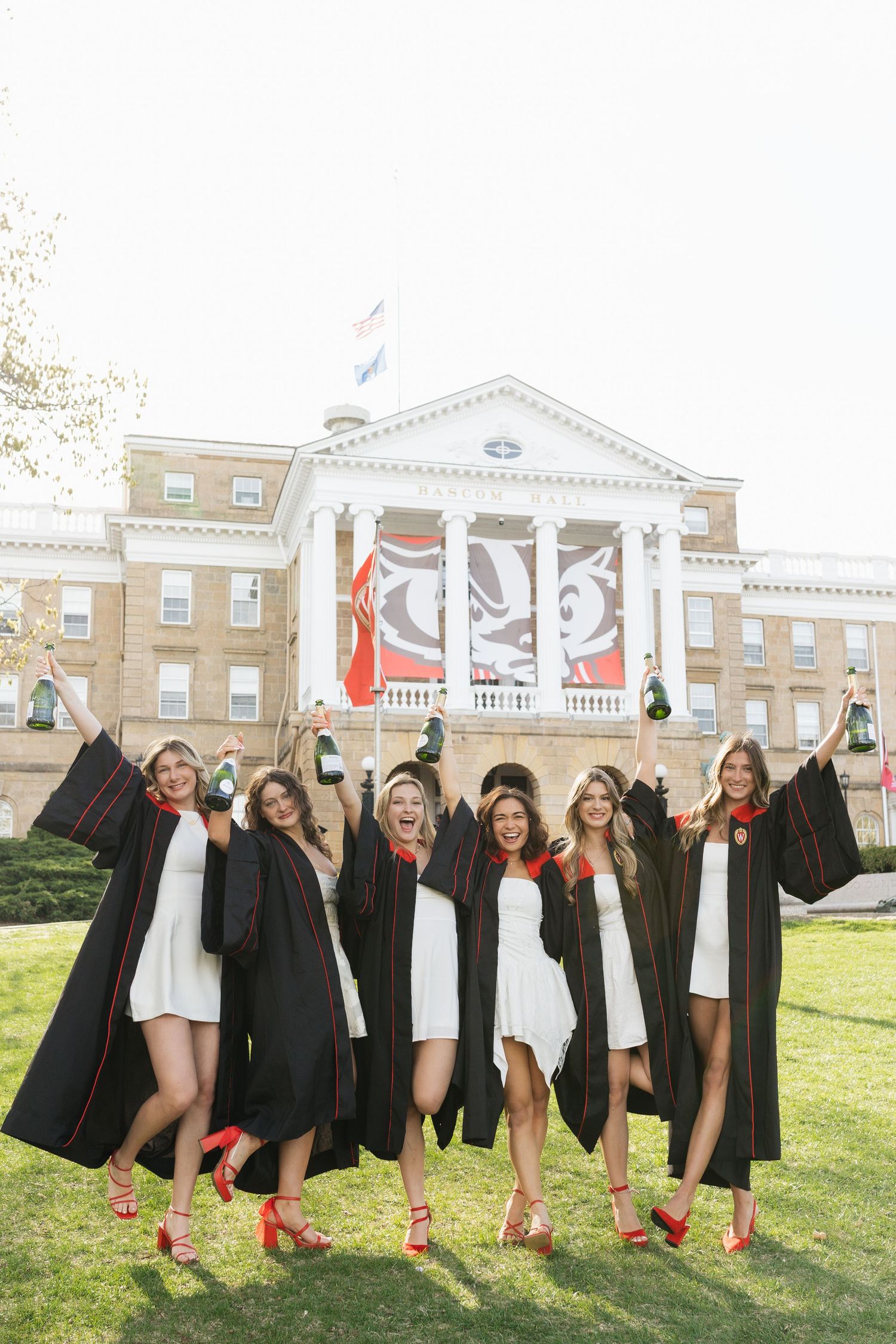 Graduates in caps and gowns celebrate on lawn in front of historic university building.