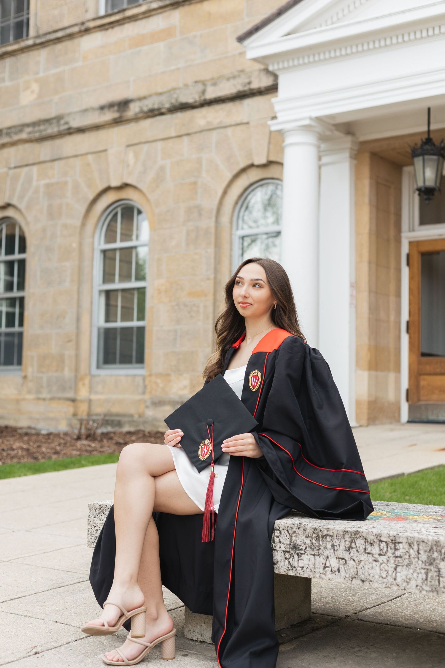 Graduate in cap and gown sitting on stone steps of historic university building.