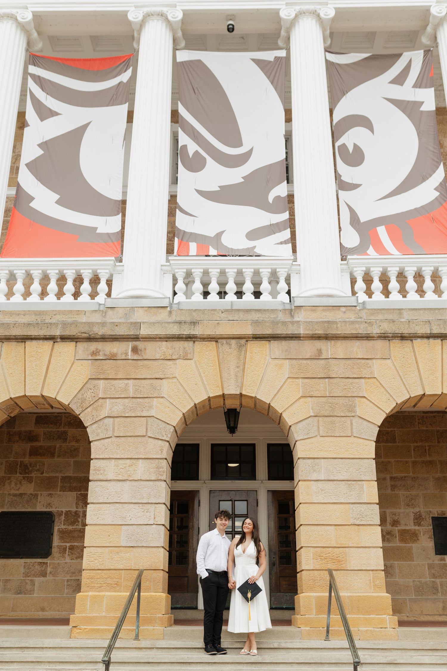 Wide view of graduates posing in front of grand university building with stone columns.