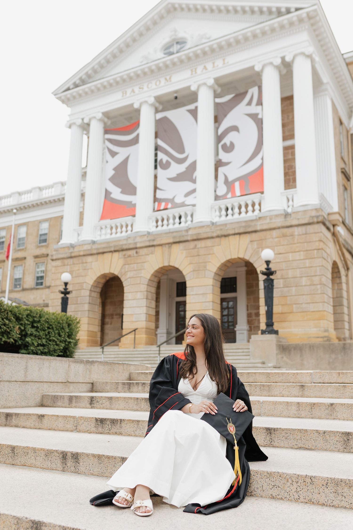 Graduate sitting on stone steps of classical university building during photo session.