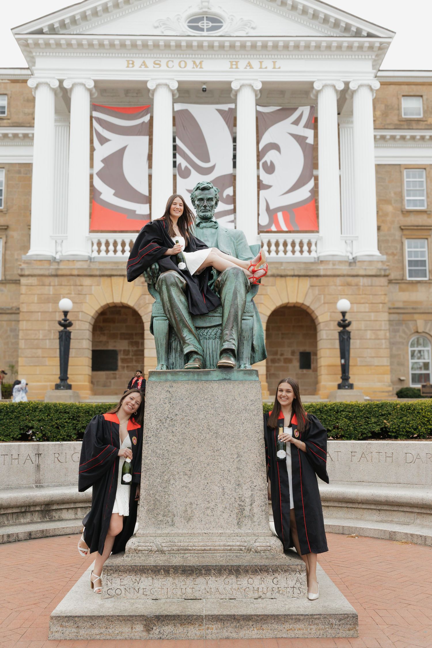 Graduates pose playfully with a bronze statue in front of Bascom Hall at University of Wisconsin-Madison.