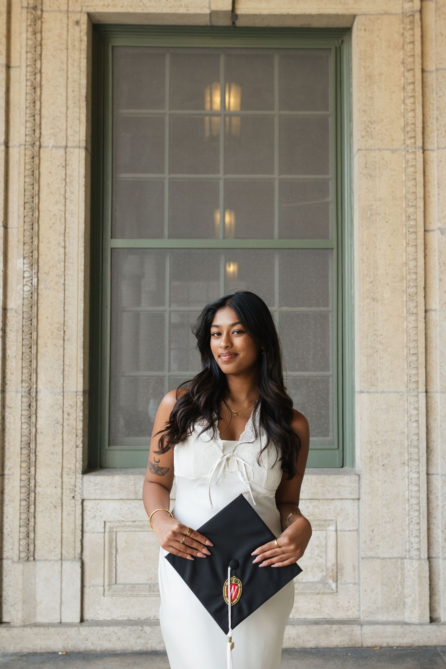 Graduate holds diploma while standing in front of classic architectural window.