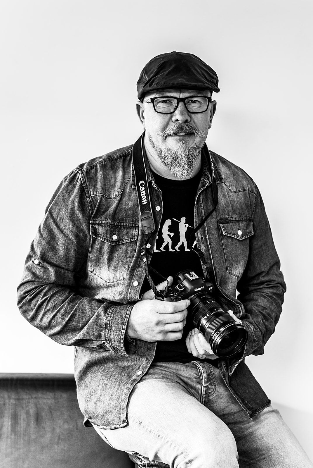 Black and white portrait of a Rob Kirman in a cap holding a Canon camera.