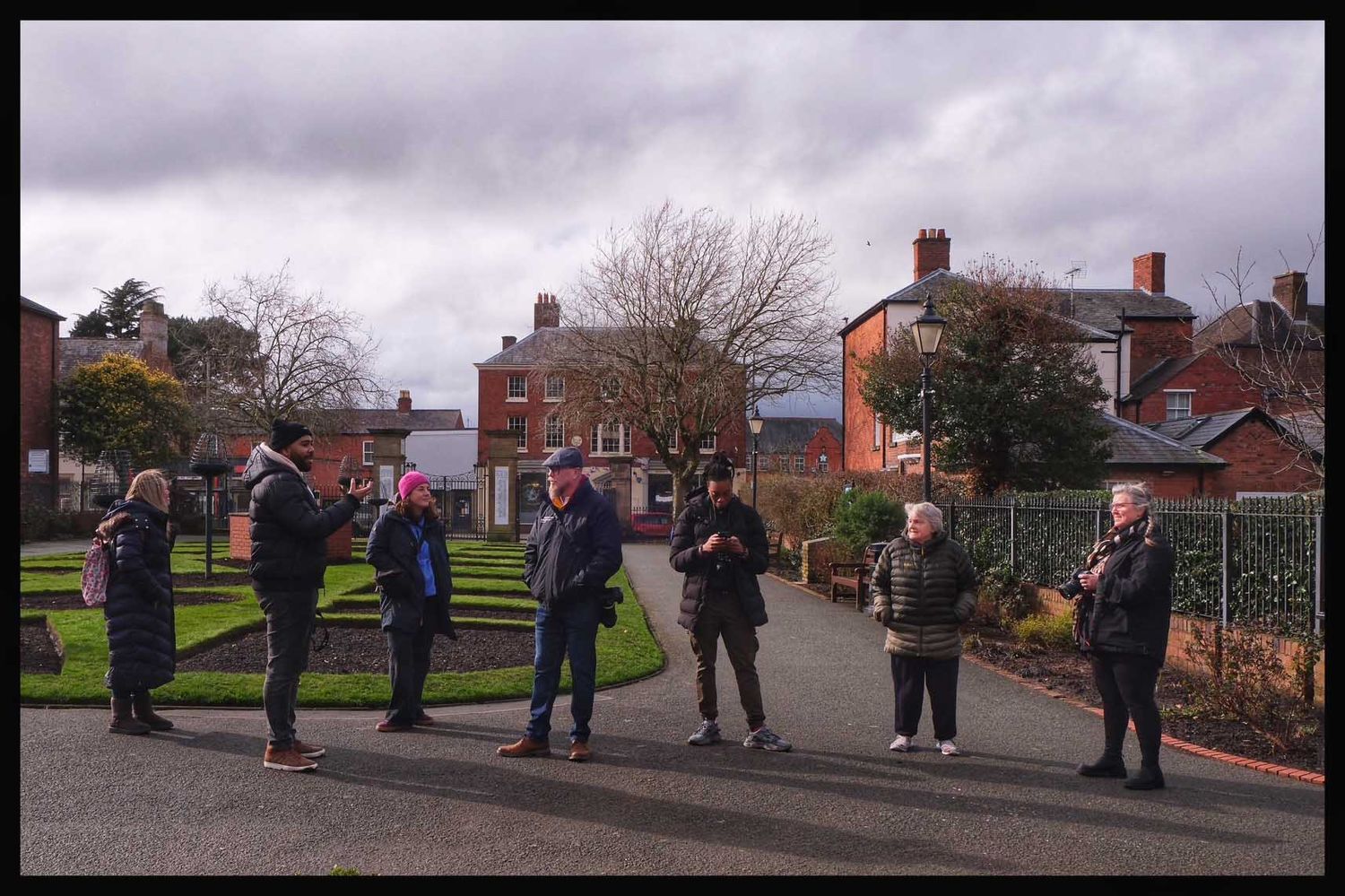 Rob Kirman with a group of students with cameras stand on a path in a park under cloudy skies.