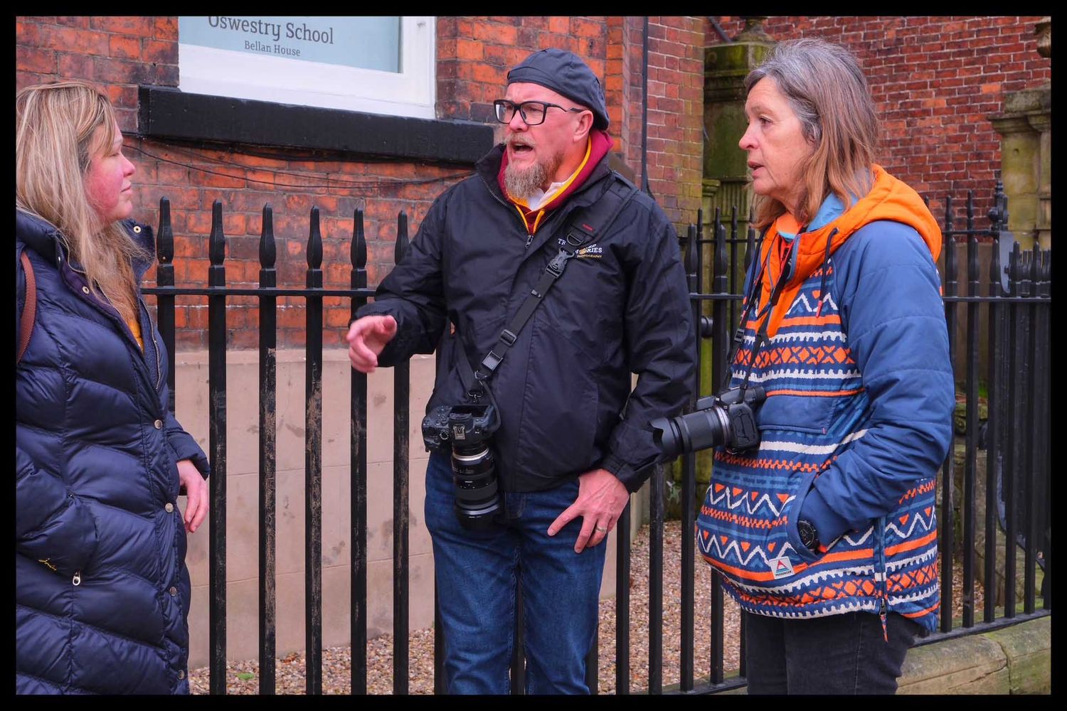 Rob Kirman and two students with cameras engage in conversation outside a historic brick building.