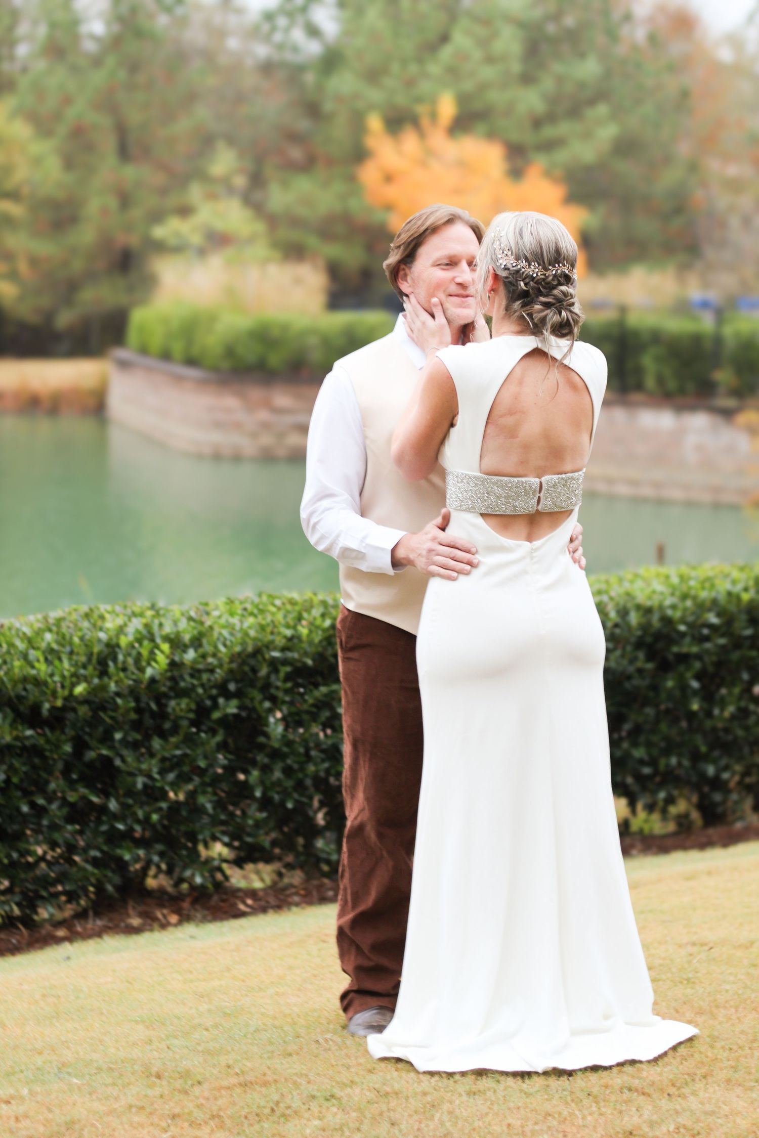 A couple shares their first look moment in formal attire by a lakeside garden.