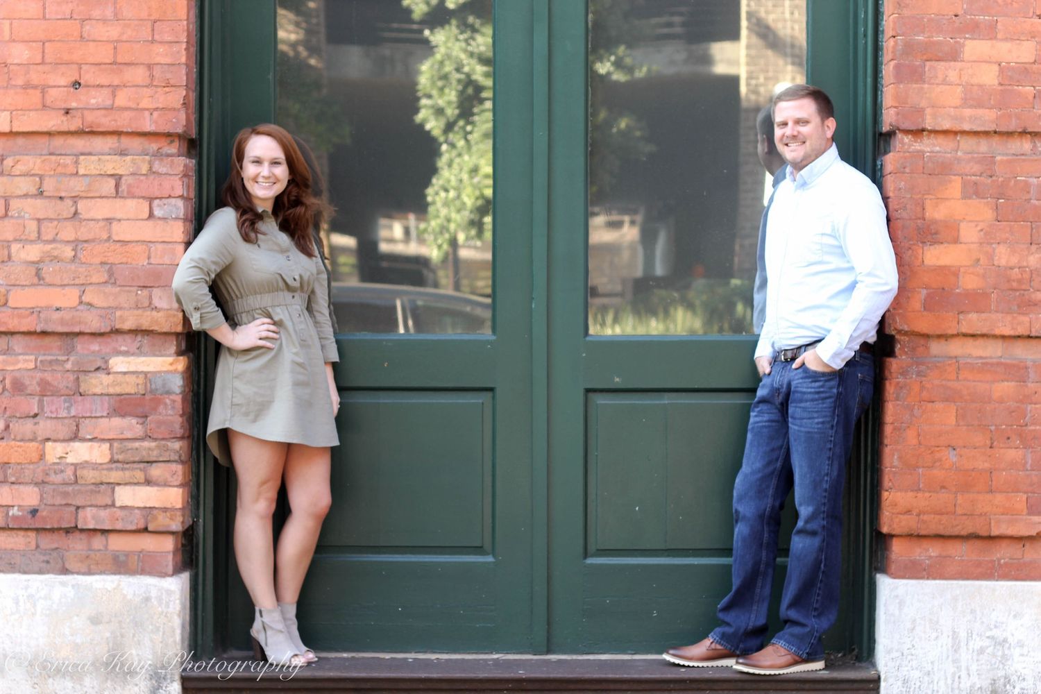 A couple shares tender moments in front of a brick building with green doors.
