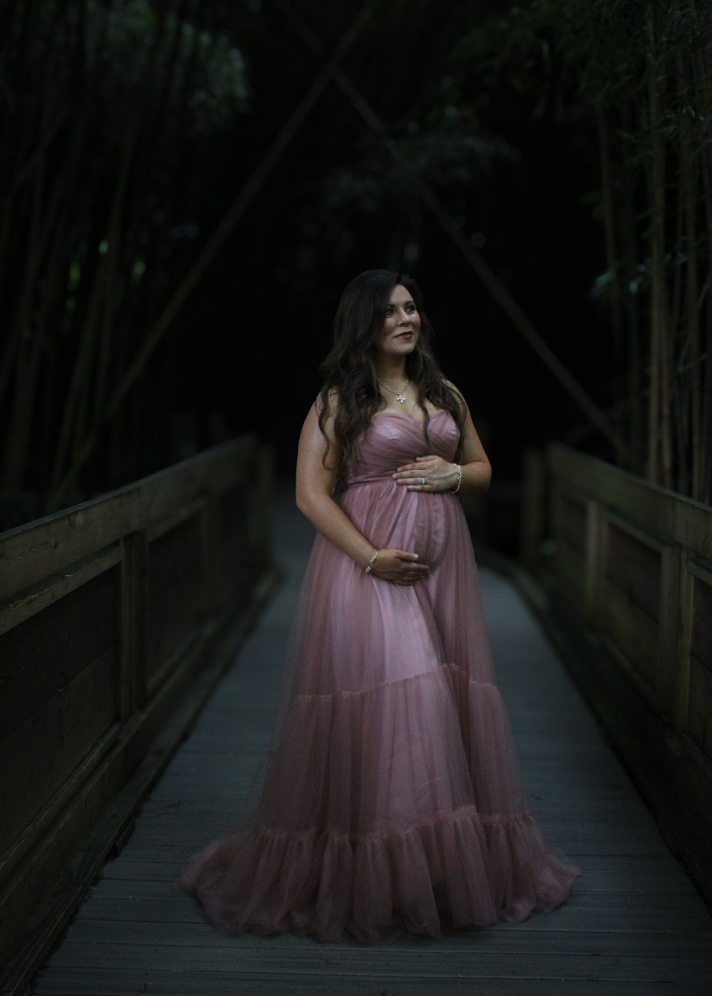 Figure in pink gown poses dramatically on dark wooden boardwalk.