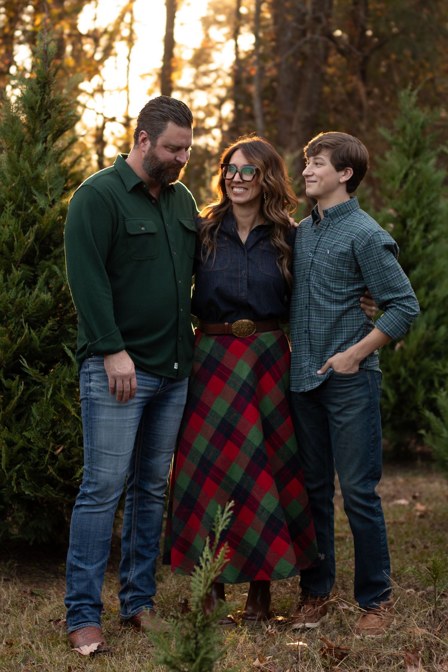 Family sharing laughs between evergreen trees in casual winter attire.