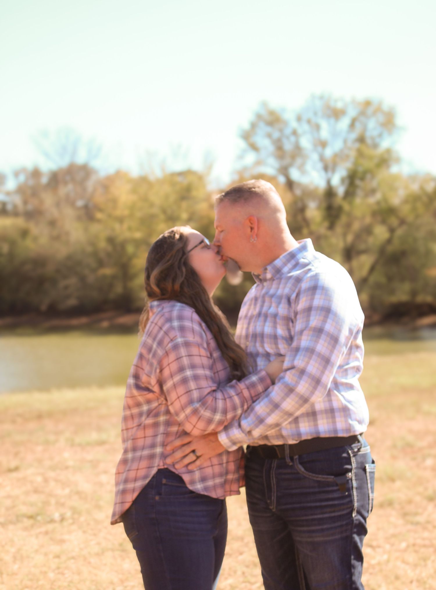 A loving couple shares intimate moments in a sunlit field wearing matching plaid shirts.