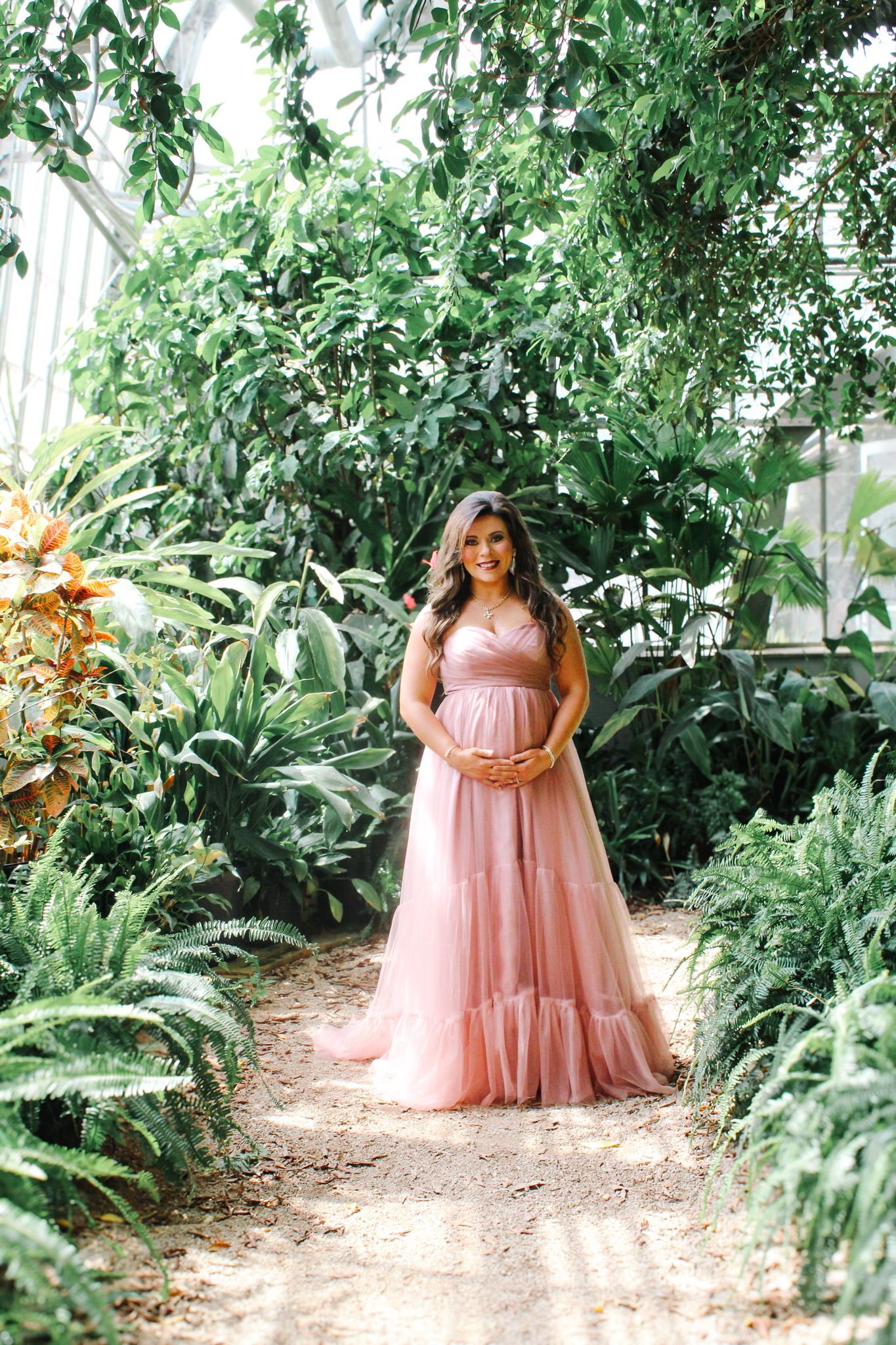 A dreamy garden maternity session featuring a flowing pink dress among lush tropical plants.