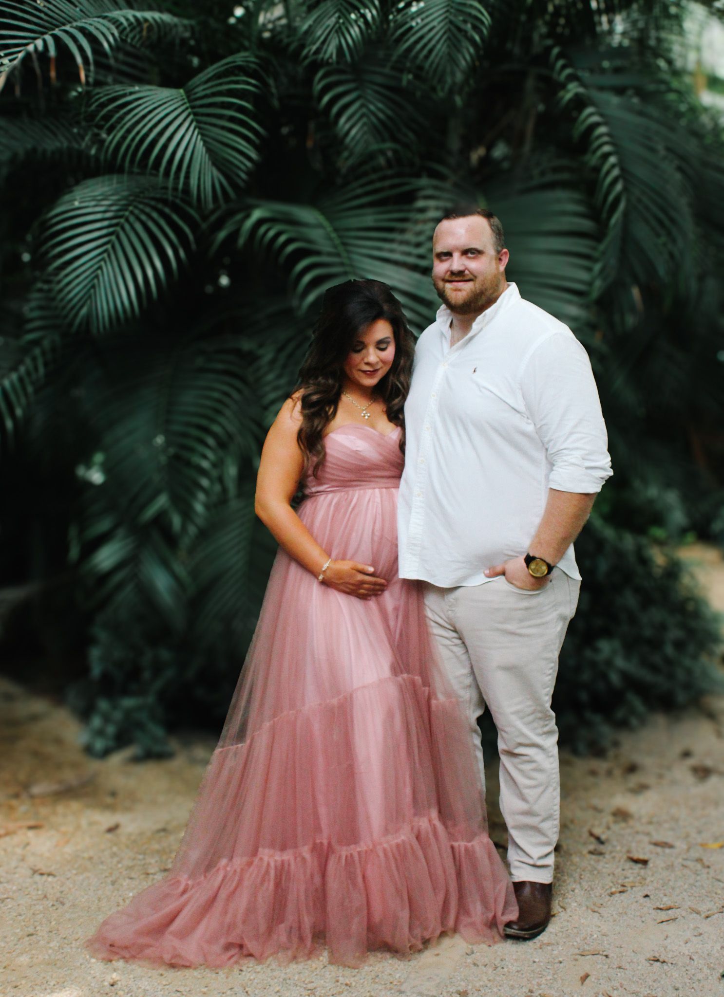 A romantic couple's maternity portrait against a backdrop of tropical palm fronds.