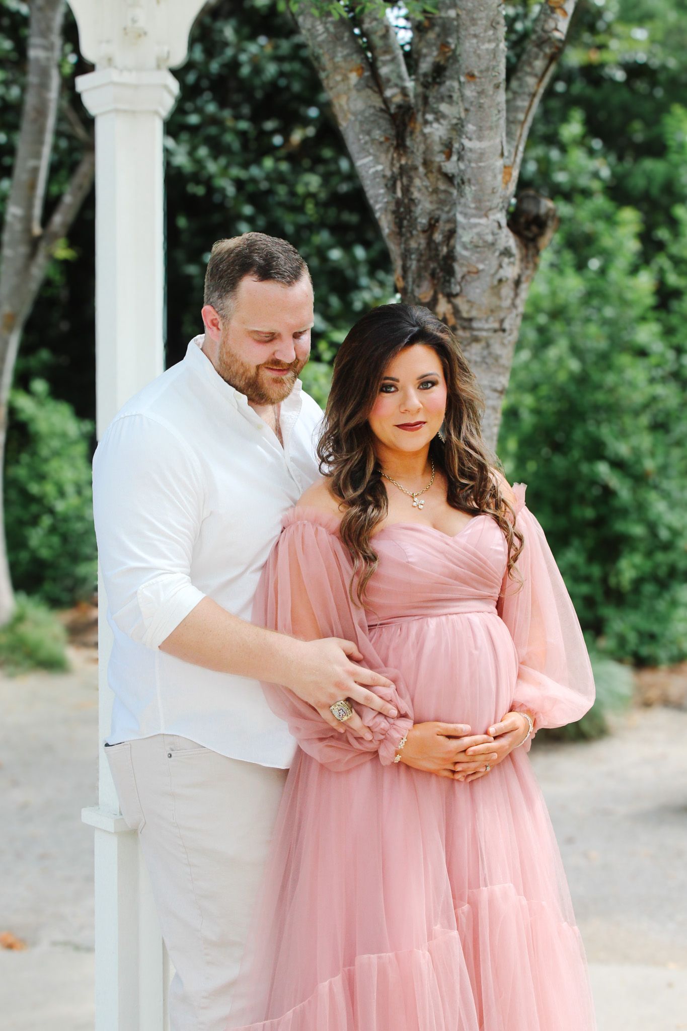 A romantic maternity portrait with a couple in pink and white attire standing together outdoors.