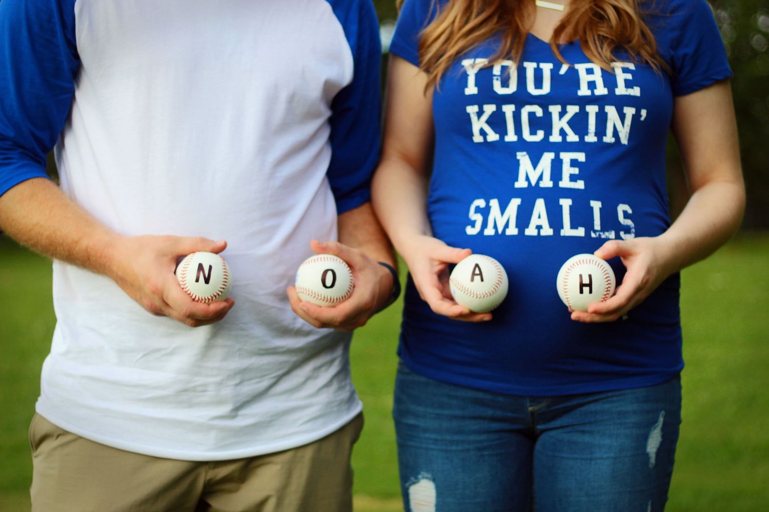 Two people hold baseballs spelling NOAH while wearing coordinating shirts for pregnancy announcement.