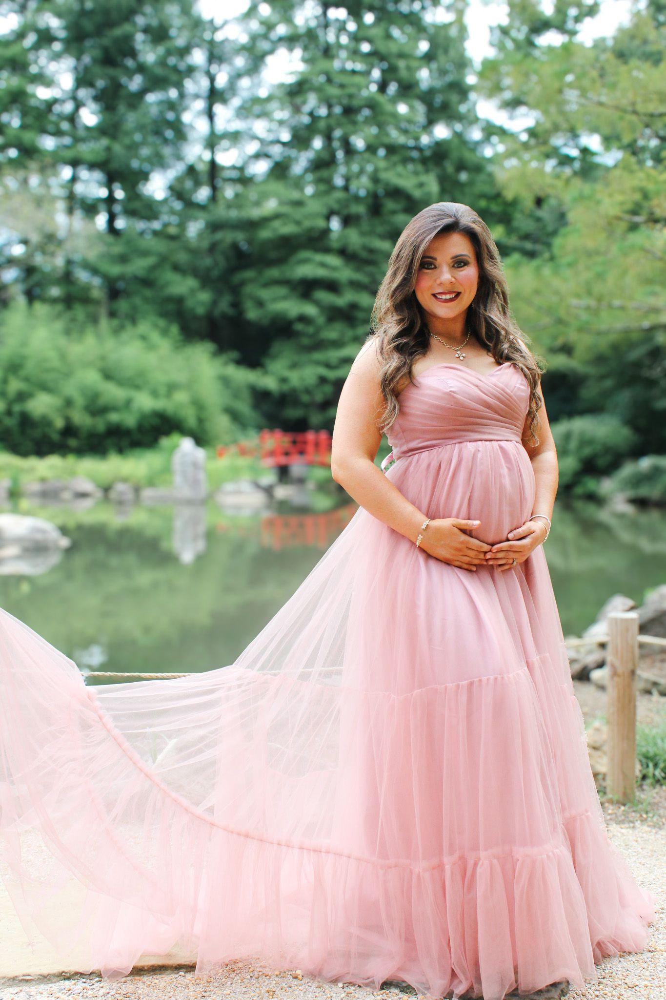 A whimsical maternity photoshoot by a pond featuring a billowing pink princess-style dress.