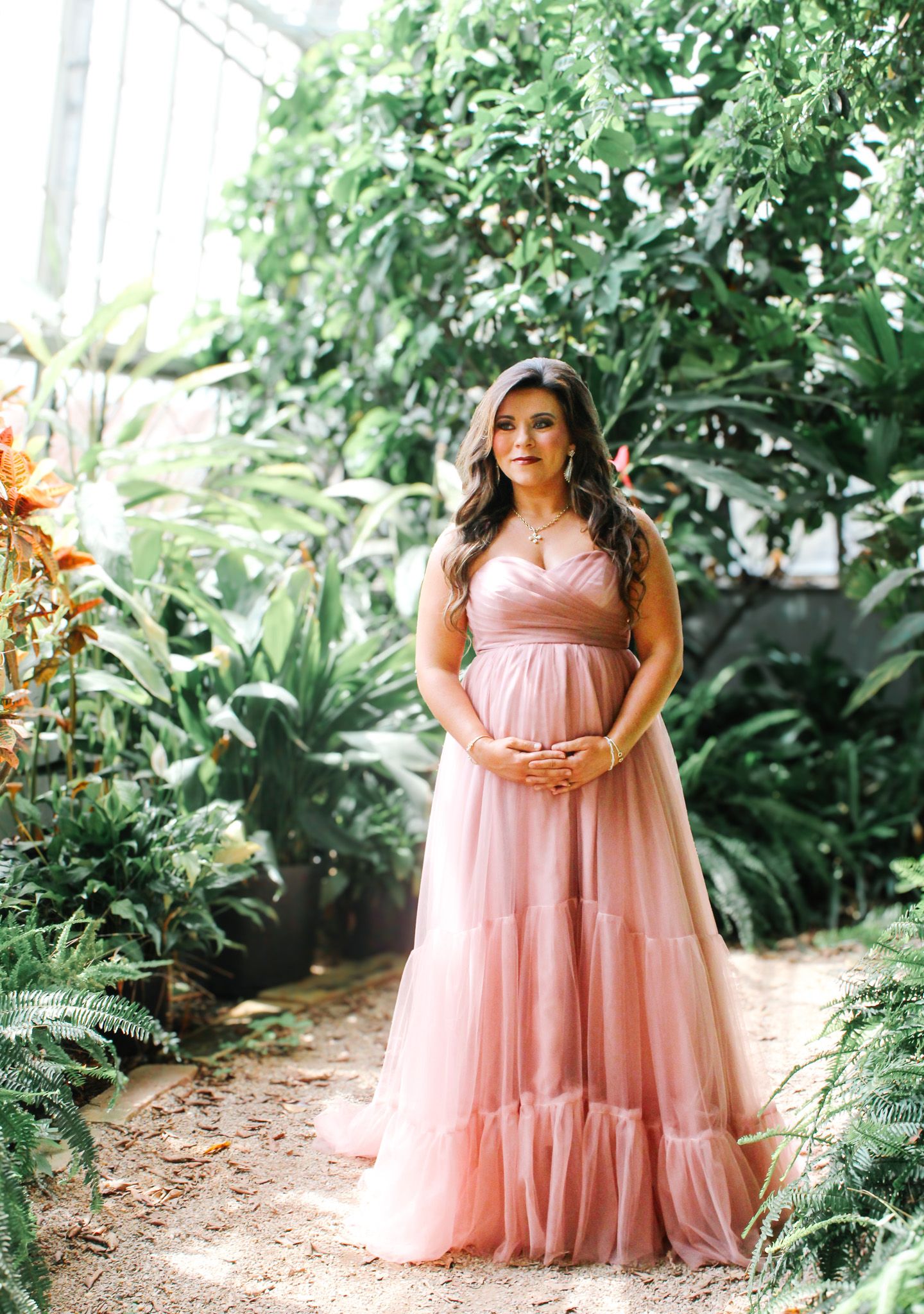 An ethereal maternity photo series in a garden path with a flowing blush pink gown.