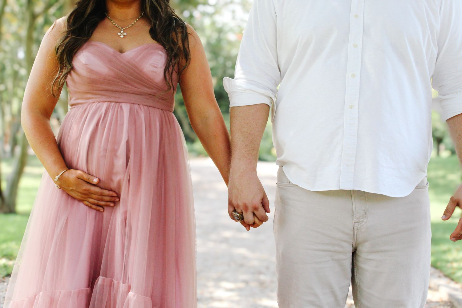 Sweet maternity moments captured outdoors with a couple in coordinating pink and white outfits.