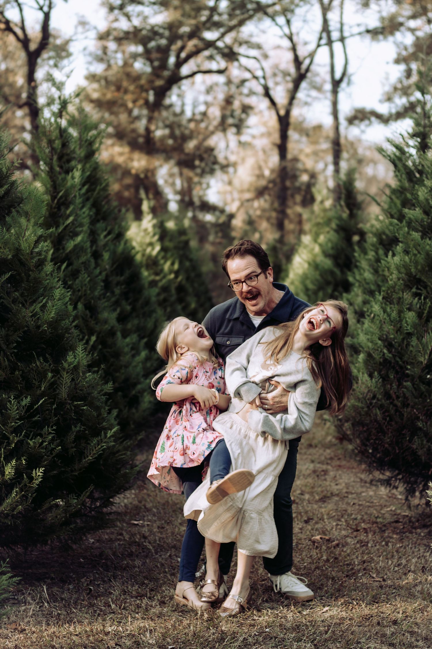 Playful family moment captured between evergreen trees during autumn.