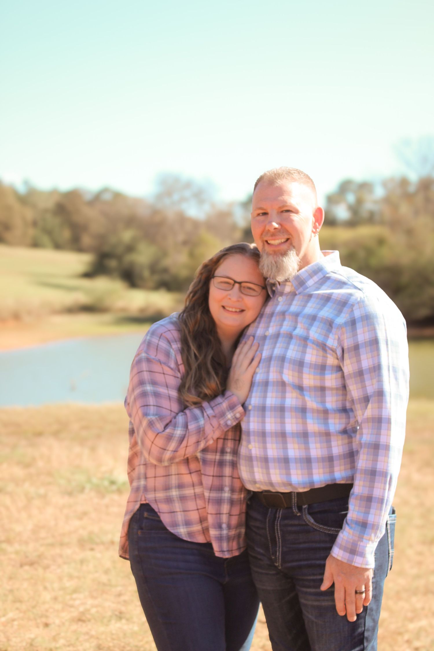 A couple embraces in a sunny field during an outdoor photo session.