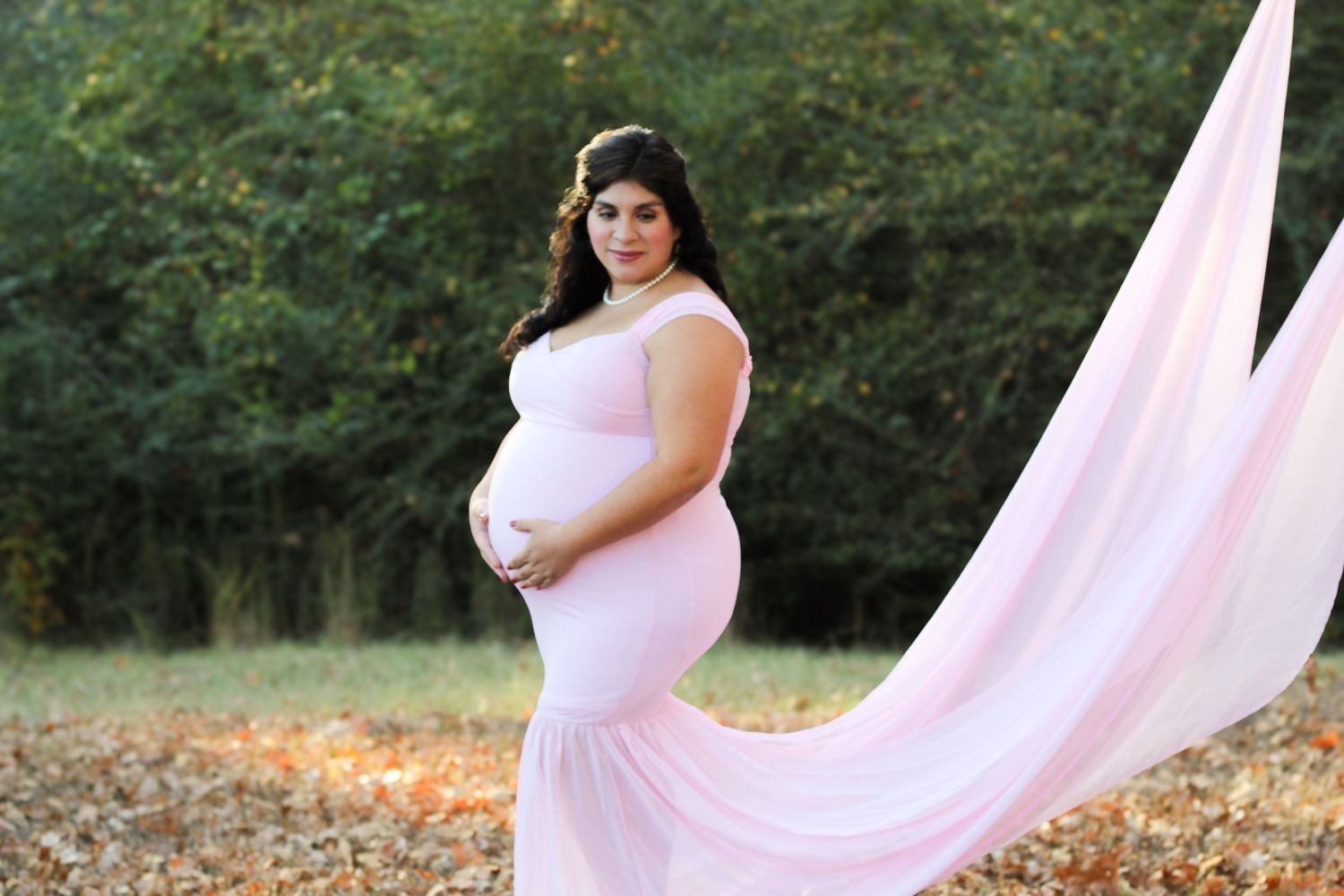 Maternity photo session in flowing pink dress during sunset in a grassy field.