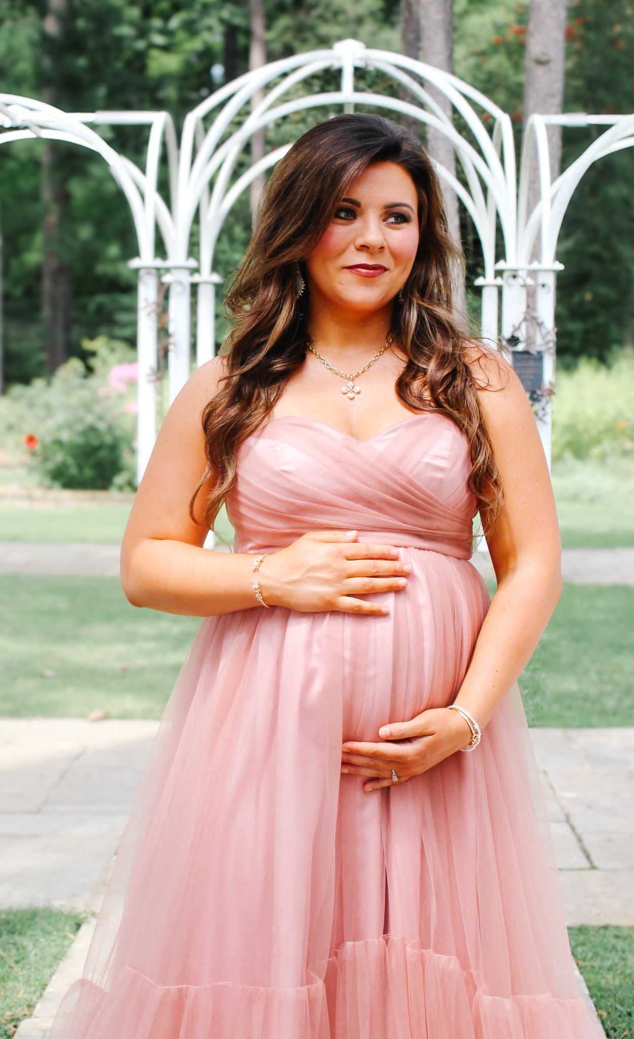 A collection of elegant maternity poses in a pink tulle gown at a garden venue.
