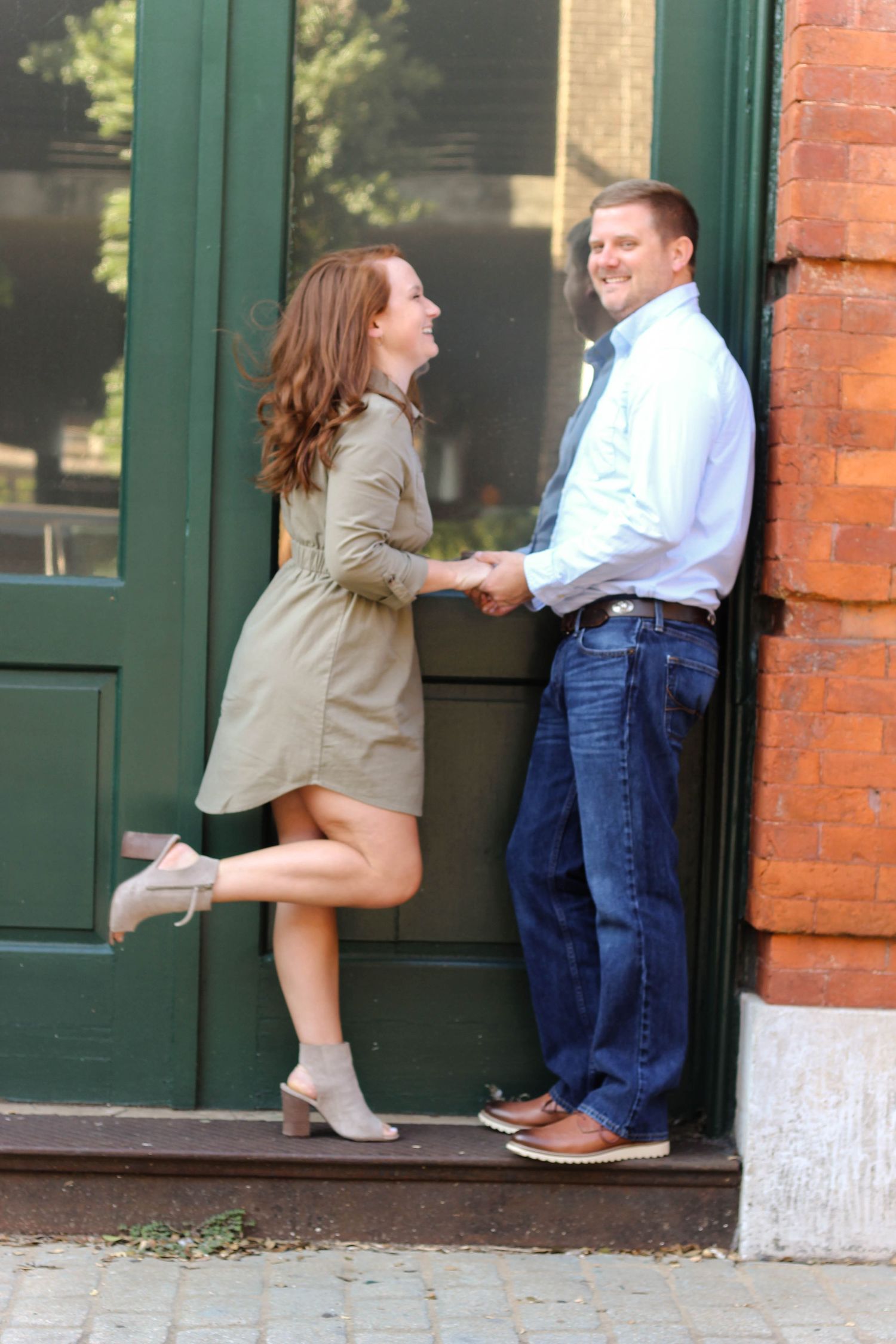 Playful engagement photo session against brick building with green door.